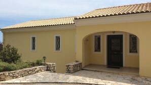 A yellow building with a tiled roof, a stone-paved entrance, and a black door with decorative glass panels. - Prestige Villas |  SPARTILAS | Secluded Villa 15-20 mins walk to Taverna (Spartilas)
