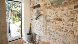 Un interior rústico con paredes de ladrillo visto, un letrero de bienvenida, un reloj y una reja metálica que da a un jardín.