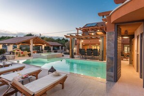 A pool area with lounge chairs and a pergola, a dining area with tables and chairs, and a building with a covered patio. - Holiday Home La Verna with Pool (Skradin)