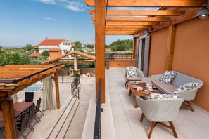 A covered outdoor seating area with a pool, wicker furniture, and a view of houses in the background. - Holiday Home La Verna with Pool (Skradin)