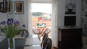 A dining area with a table, chairs, a vase of flowers, a television, and a view of buildings through a window. - Apartments Optimist (Makarska)