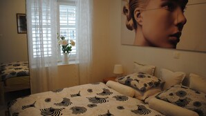A bedroom with a bed, a window with curtains, a vase with flowers, and a wall with a portrait. - Apartments Optimist (Makarska)