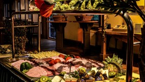 En buffet med et udvalg af madvarer, herunder kød, oste, frugt og grøntsager.