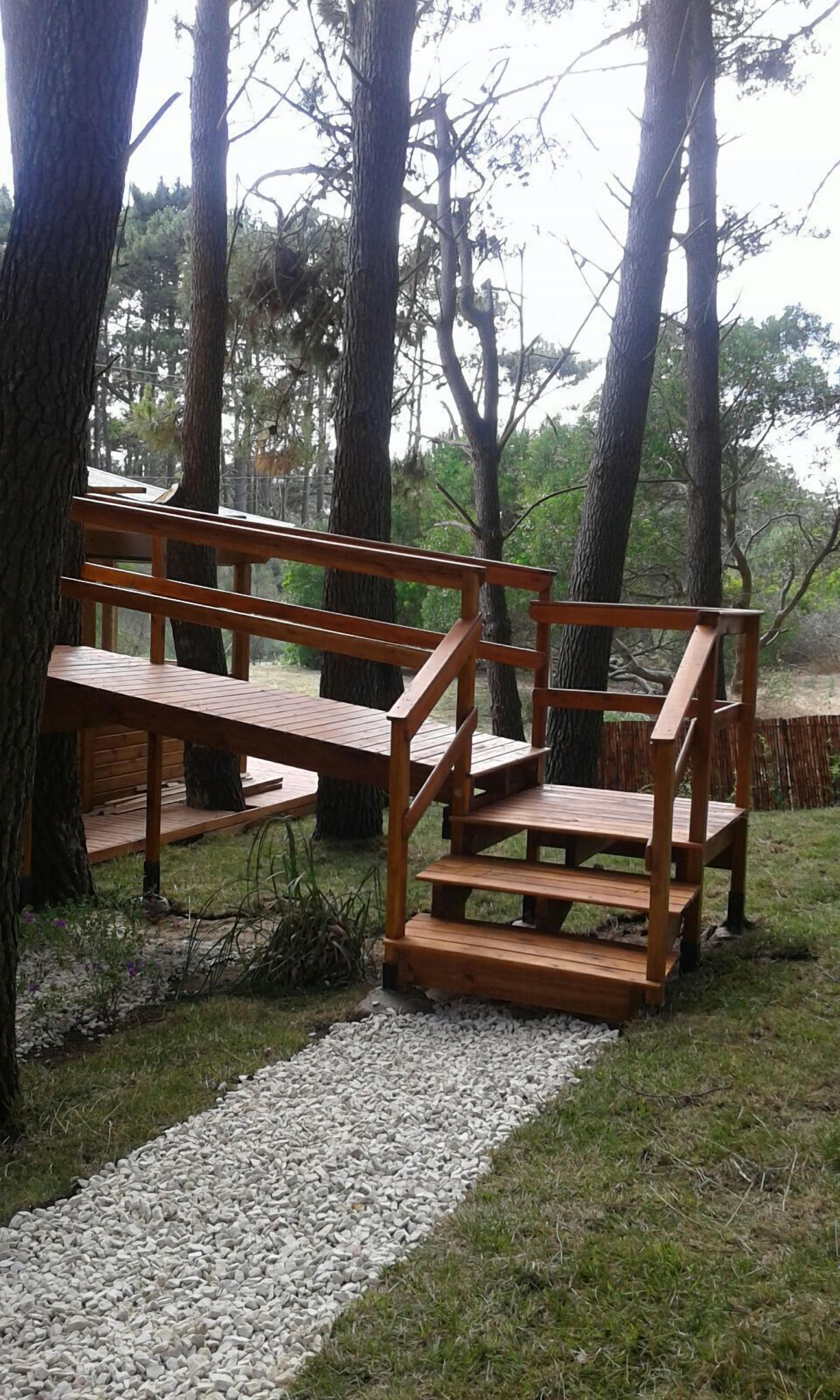 A wooden bench with a backrest and armrests, situated on a gravel path surrounded by trees.