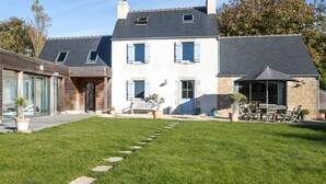 Una casa moderna con un invernadero de vidrio, un patio de piedra y un comedor con mobiliario de exterior.
