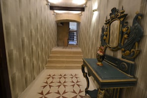 A hallway with a patterned floor, a staircase, and a decorative mirror on the wall.