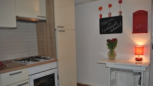 A kitchen with white cabinets, a gas stove, an oven, a small table with a vase of flowers, and a wall-mounted sign. - Apartments Optimist Split (Split)