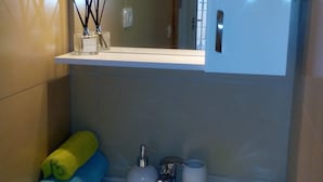 A bathroom with a white sink, a mirror above it, and a shelf with a bottle and reed diffusers. - Apartments Optimist Split (Split)