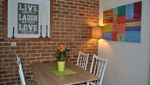 A dining area with a brick wall, a framed inspirational quote, a table with chairs, a potted plant, and a colorful wall art piece. - Apartments Optimist Split (Split)
