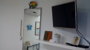 A room with a white round table, a wooden chair, a TV mounted on the wall, a shelf with a few items, and a colorful floor. - Apartments Optimist Split (Split)