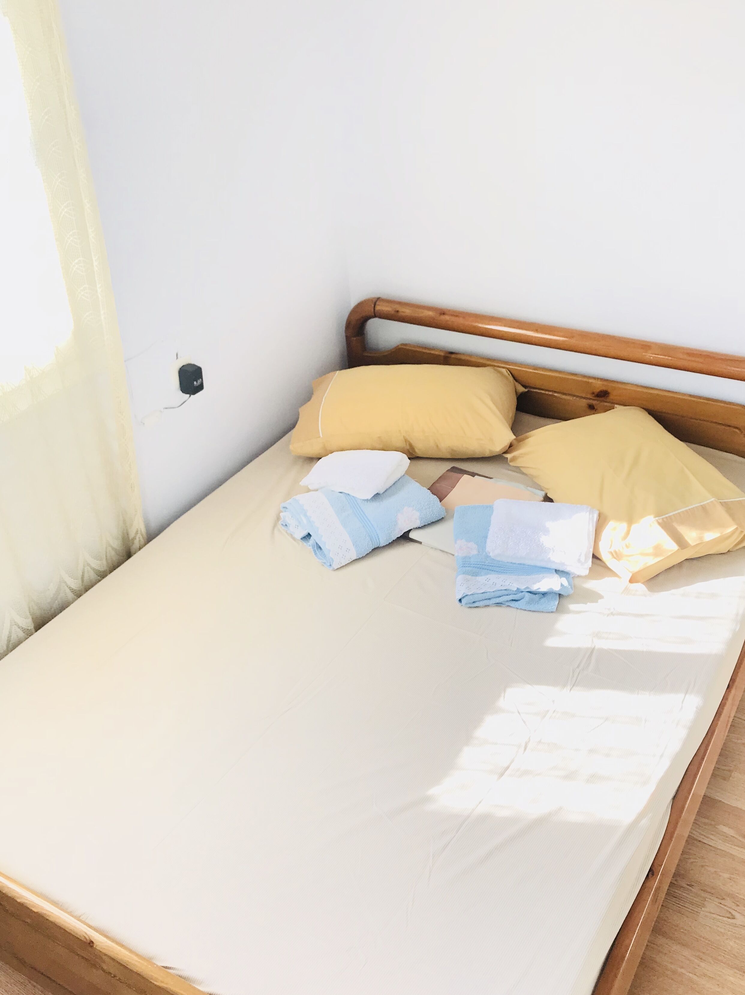 A bed with a wooden headboard, a beige mattress, and several pillows and folded towels.