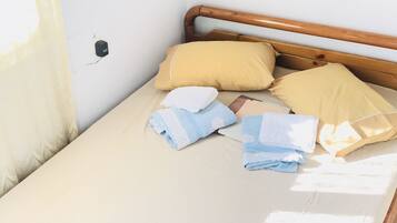 A bed with a wooden headboard, a beige mattress, and several pillows and folded towels.