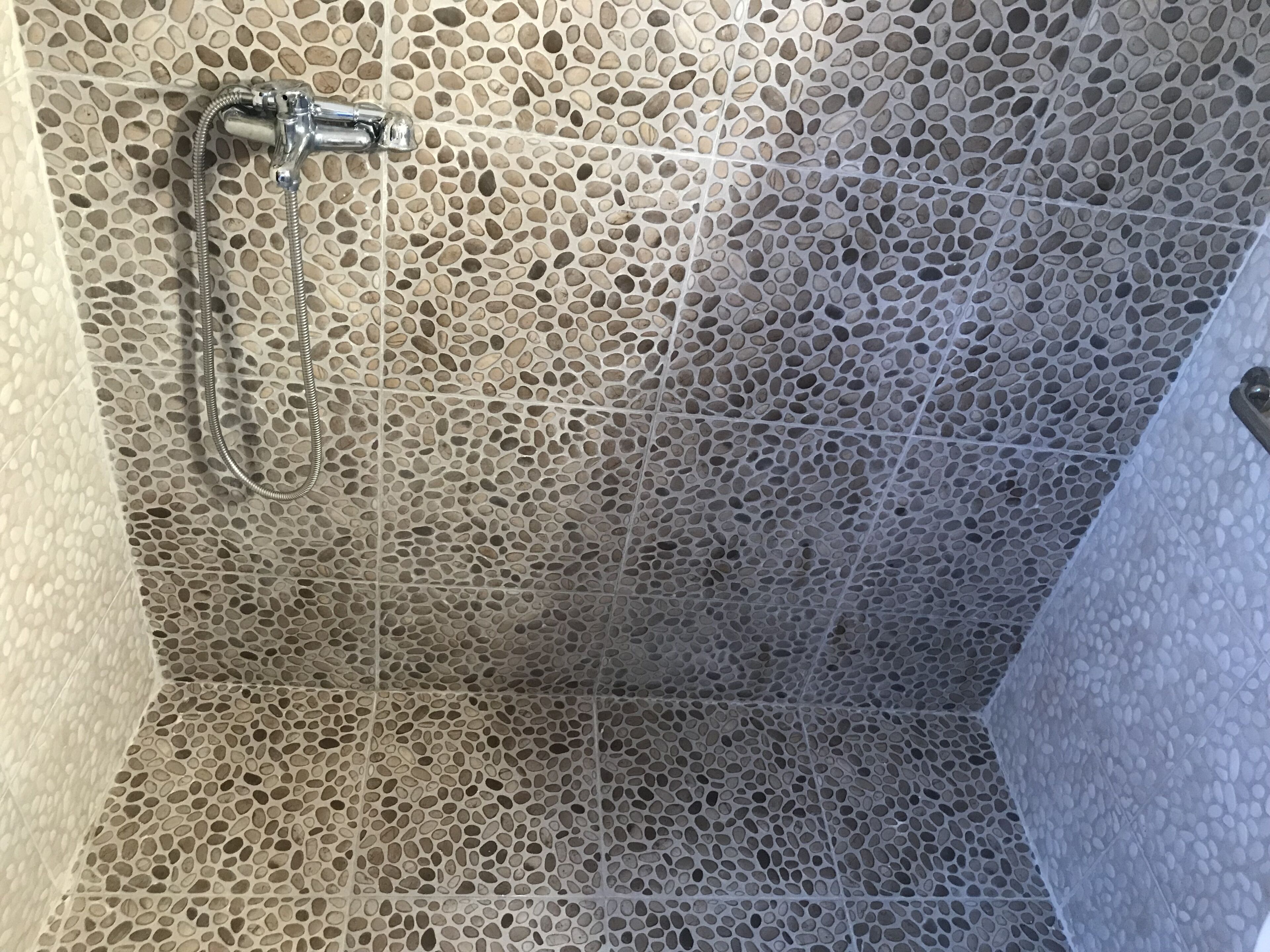 Une douche avec un mur recouvert de mosaïques et un pommeau de douche à main.