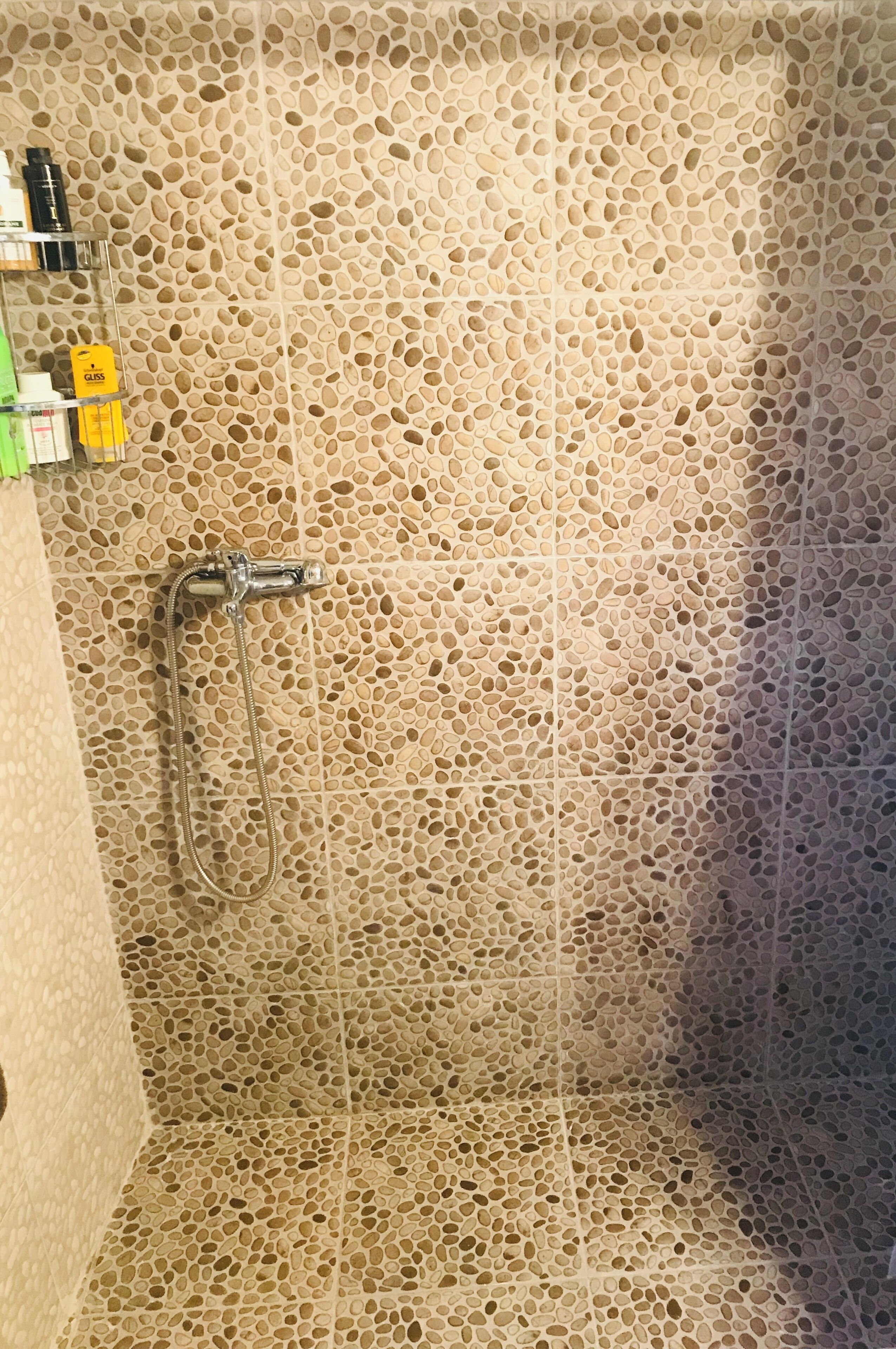 Un área de ducha con pared de azulejos perforados y ducha de mano.
