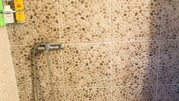 Un área de ducha con pared de azulejos perforados y ducha de mano.