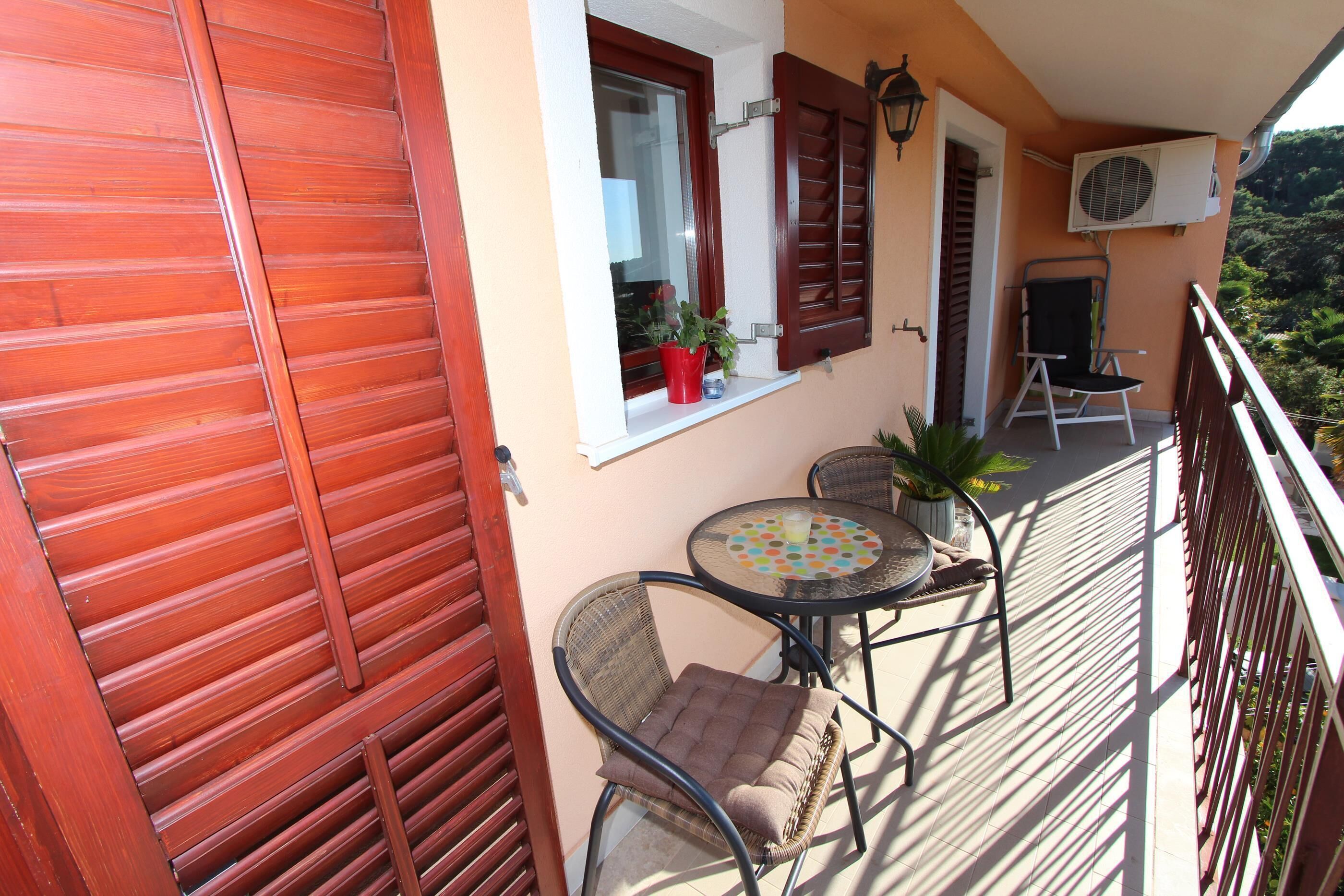 A balcony with a wooden railing, a table with chairs, a potted plant, and an air conditioning unit.