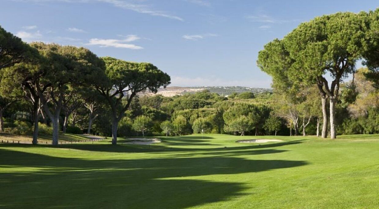 A golf course with a well-maintained green, sand bunkers, and mature trees.