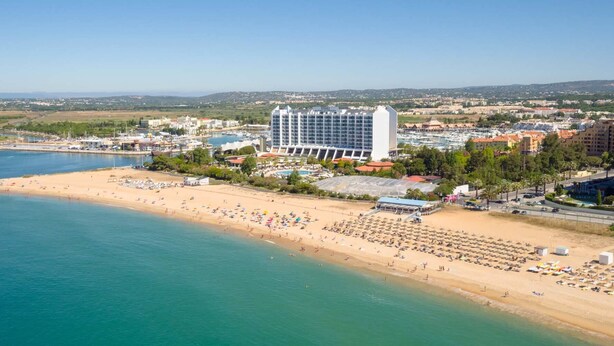 Un hôtel en bord de mer offrant une vue sur la plage, plusieurs piscines et un port de plaisance.