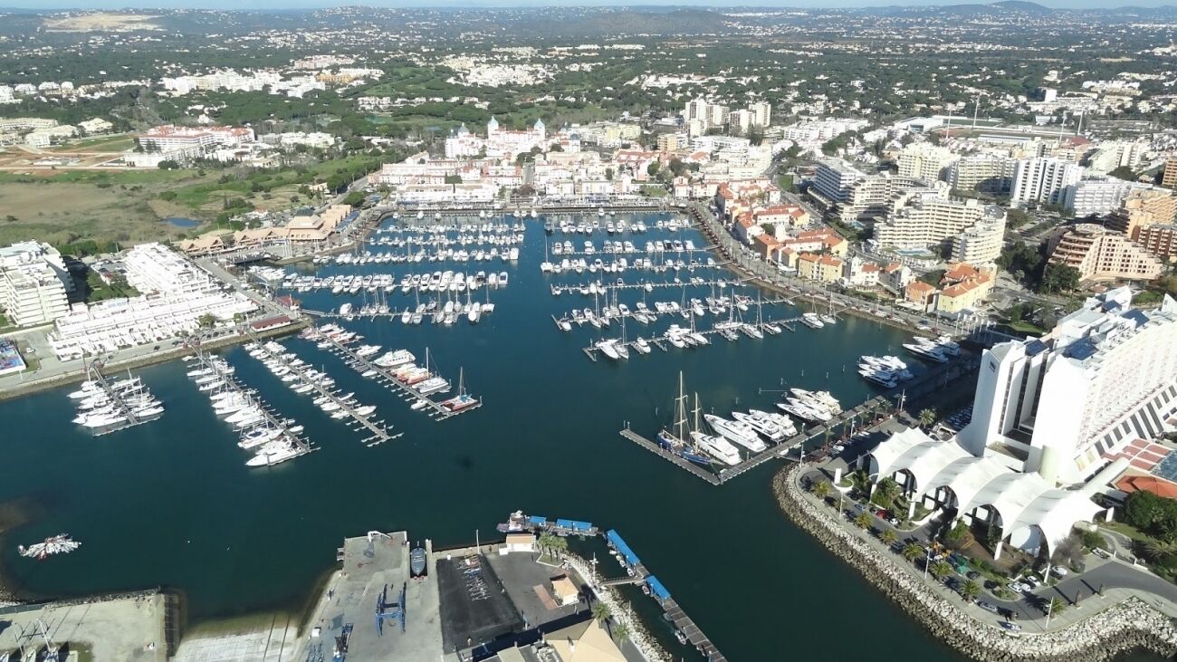 Vue aérienne d’une marina où sont amarrés de nombreux bateaux, entourée de bâtiments et de verdure.