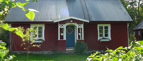 A red wooden house with a blue door, white window frames, and a metal roof.