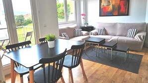 Ein modernes Wohnzimmer mit einer Couch, einem Esstisch mit Stühlen und einem großen Fenster mit Blick ins Freie.