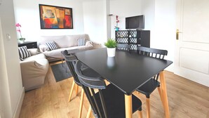 Ein modernes Wohnzimmer mit einer Couch, einem Esstisch mit Stühlen, einem Fernseher und einer Zierpflanze.