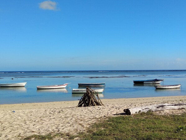 En strand med flere både forankret i rolige farvande, en sandet kystlinje og en klar himmel.