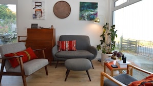 A living room with a grey sofa, a wooden cabinet, and a window with a view of a garden.