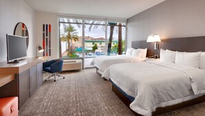 A hotel room with two beds, a TV, a desk, a chair, and a view of palm trees and a building outside. - Hampton Inn  & Suites Anaheim Resort Convention Center (Anaheim)
