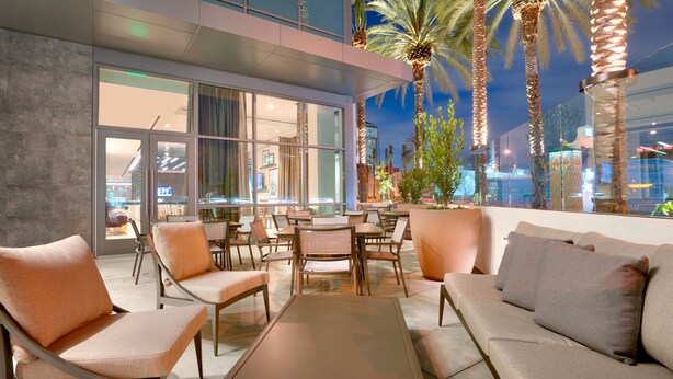 An outdoor seating area with modern furniture, large windows, and palm trees. - Hampton Inn  & Suites Anaheim Resort Convention Center (Anaheim)