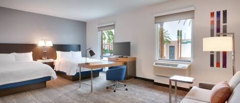 A hotel room with a bed, desk, chair, and a couch.