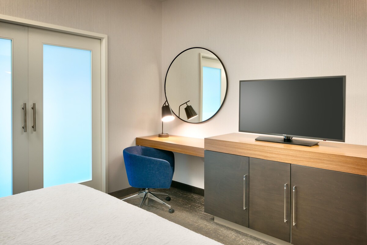 Une chambre d’hôtel comprenant un lit, un bureau avec une télévision, une chaise, une lampe de bureau et un miroir.