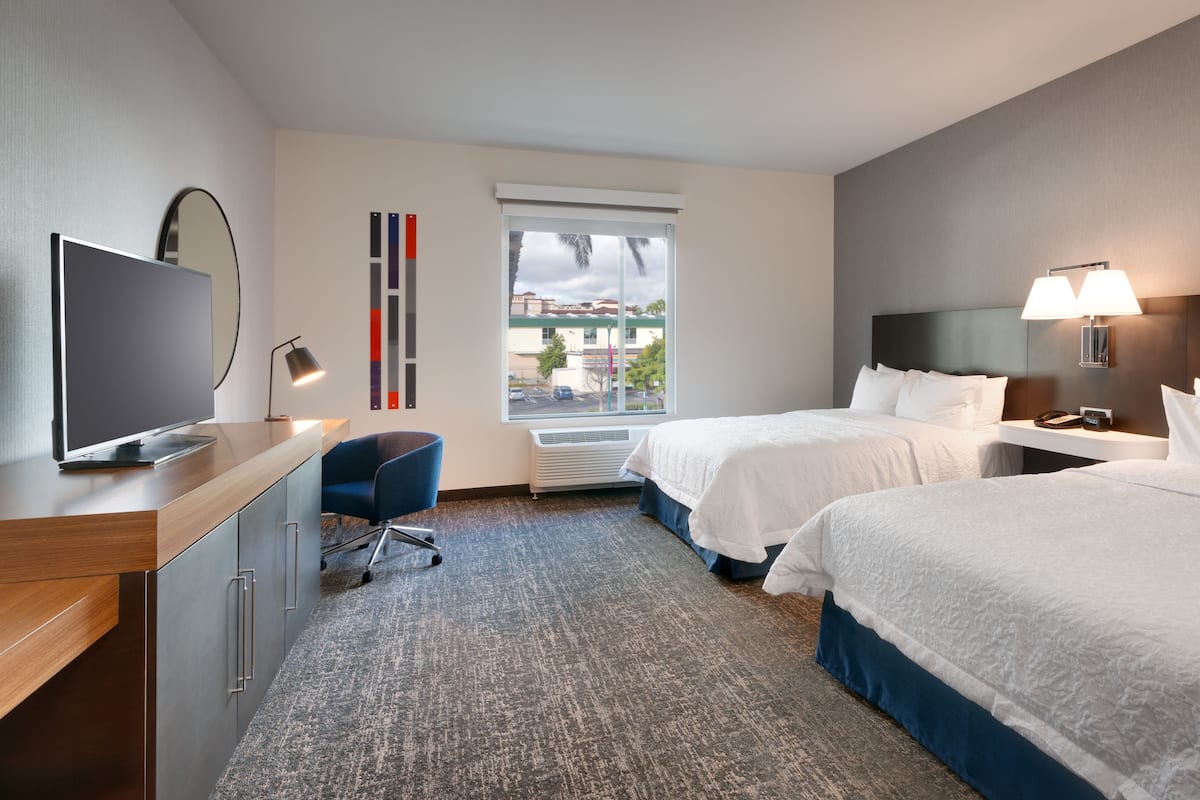 Une chambre d’hôtel avec deux lits, un bureau avec une télévision, une chaise, une fenêtre donnant sur un paysage agréable et une lampe.