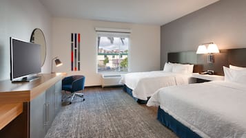 A hotel room with two beds, a desk with a TV, a chair, a window with a view, and a lamp.