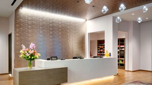 A modern hotel reception area with a wooden reception desk, a floral centerpiece, and a visible minibar. - Hampton Inn  & Suites Anaheim Resort Convention Center (Anaheim)