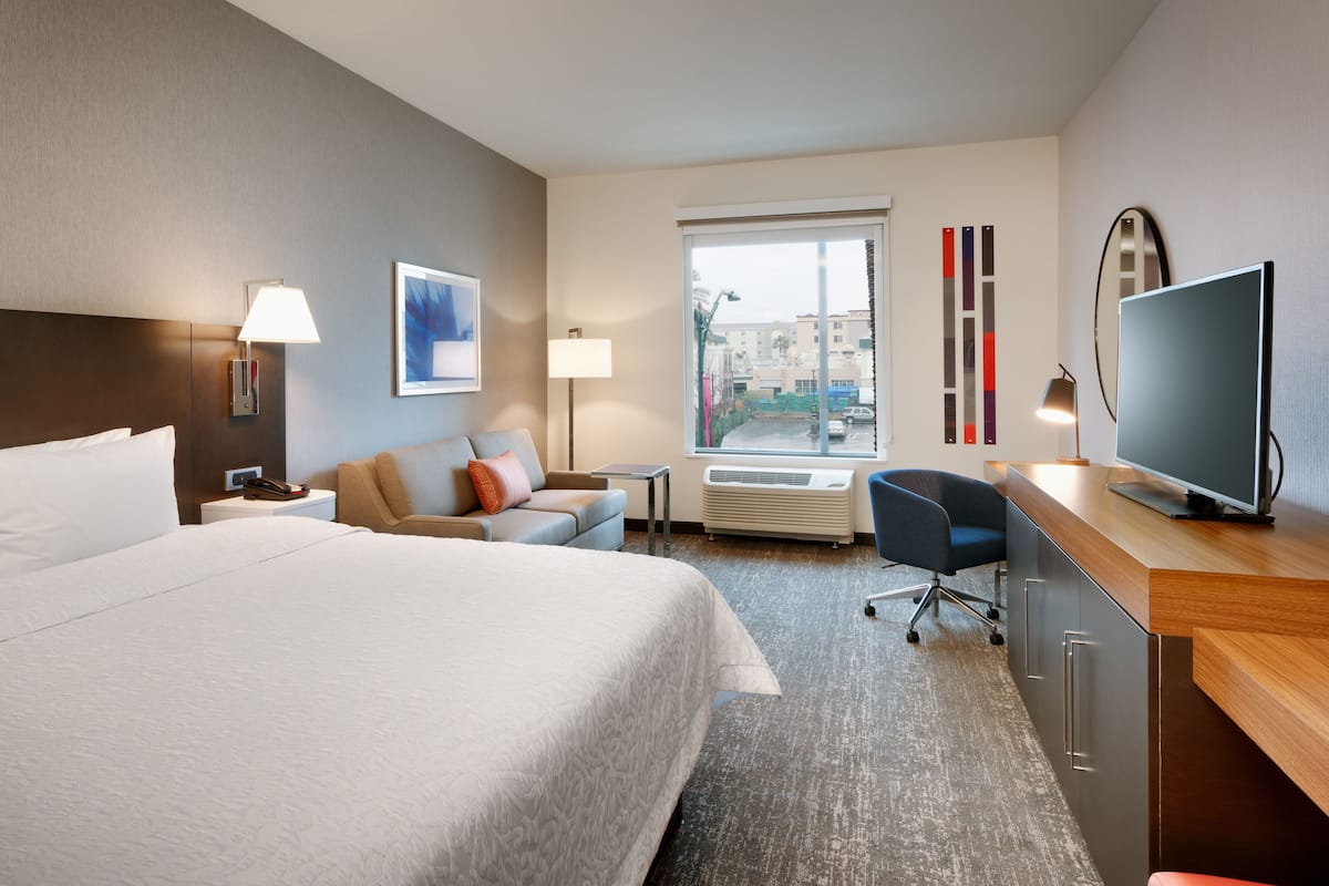 Une chambre d’hôtel avec un grand lit, un bureau doté d’un téléviseur à écran plat, un canapé, une petite table et une fenêtre donnant sur des immeubles.