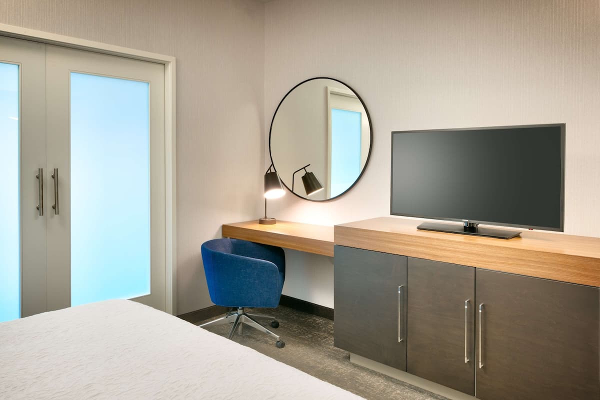Une chambre d’hôtel avec un lit, un bureau avec une télévision, une chaise et un miroir.