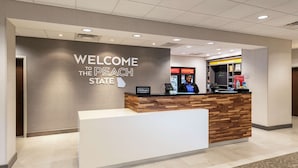 Un mostrador de recepción con un cartel que dice “Welcome to the Peach State”, una encimera de madera y una zona de minibar.