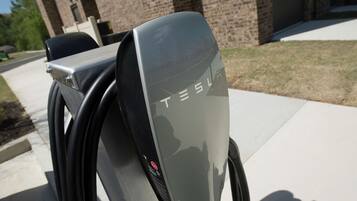 Estação de carregamento para veículos elétricos Tesla com um edifício de tijolos ao fundo.