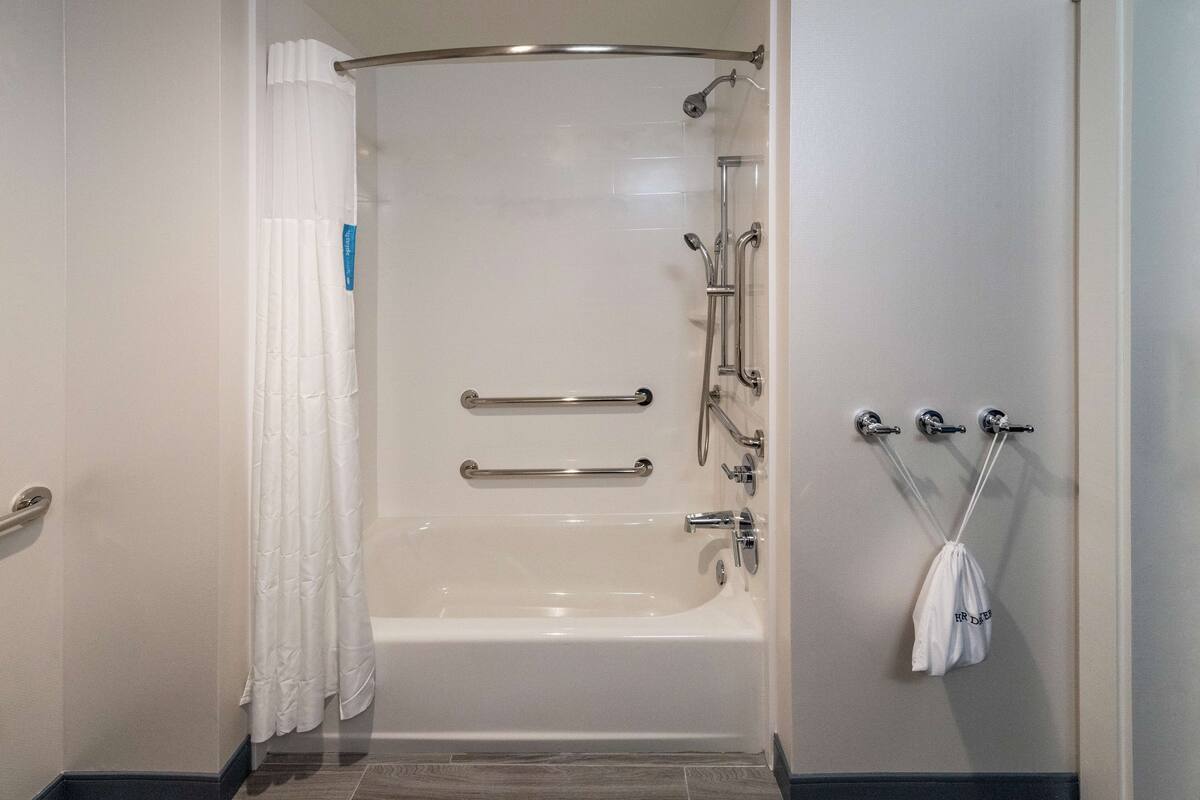 A modern bathroom with a bathtub, shower, and handrails.