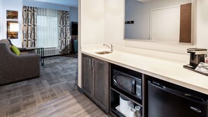 Una habitación de hotel moderna con kitchenette, un espejo grande, un sofá y vistas a la ciudad.