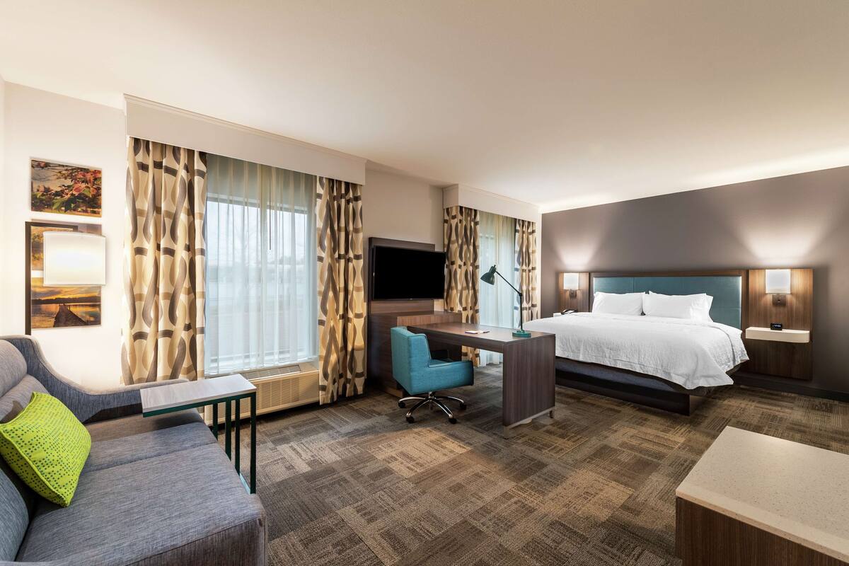 A hotel room with a bed, a desk, a chair, a TV, and a couch.
