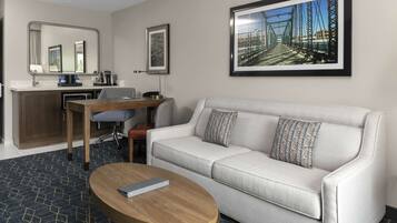 Ein Hotelzimmer mit Sofa, Couchtisch, Schreibtisch mit Stuhl, Spiegel und einem gerahmten Bild an der Wand.
