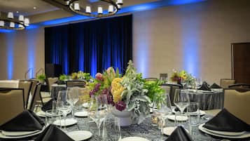 A banquet table set for a formal event with a floral centerpiece, arranged chairs, and a stage in the background.