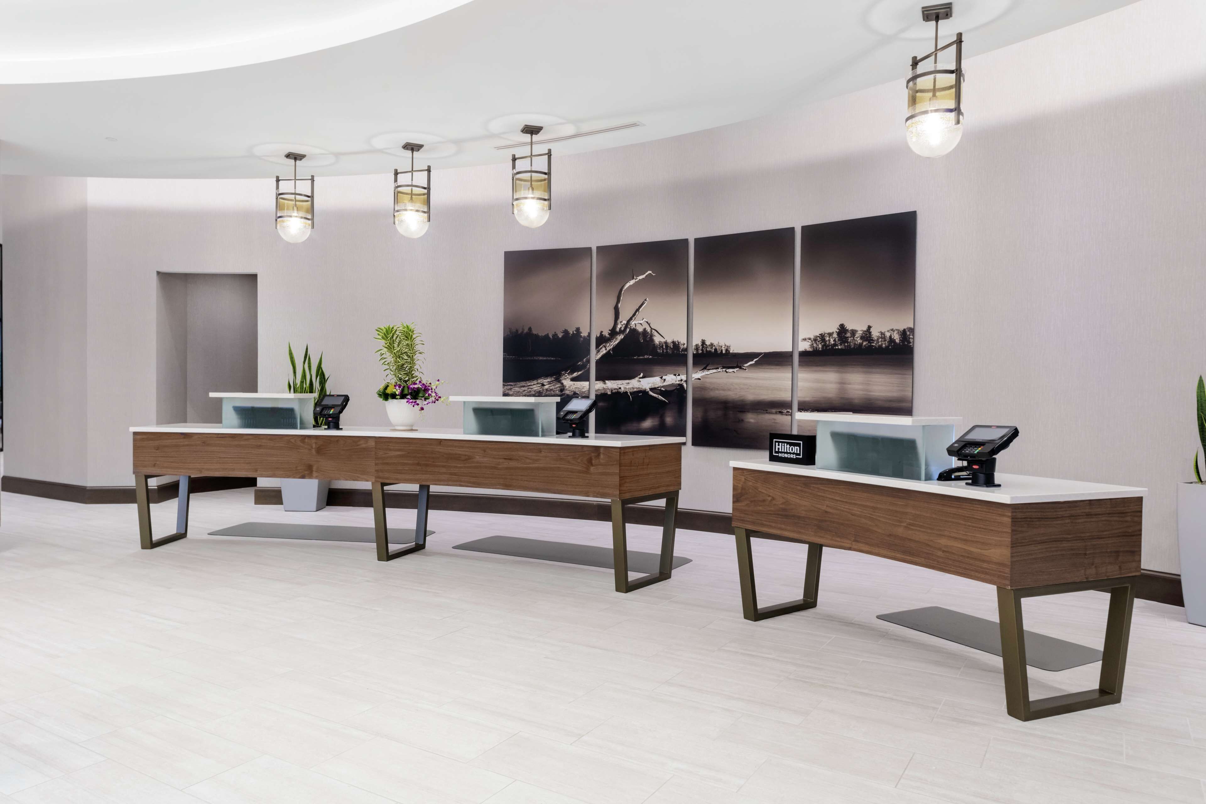 A modern reception area with two reception desks, a large landscape painting, and a potted plant.