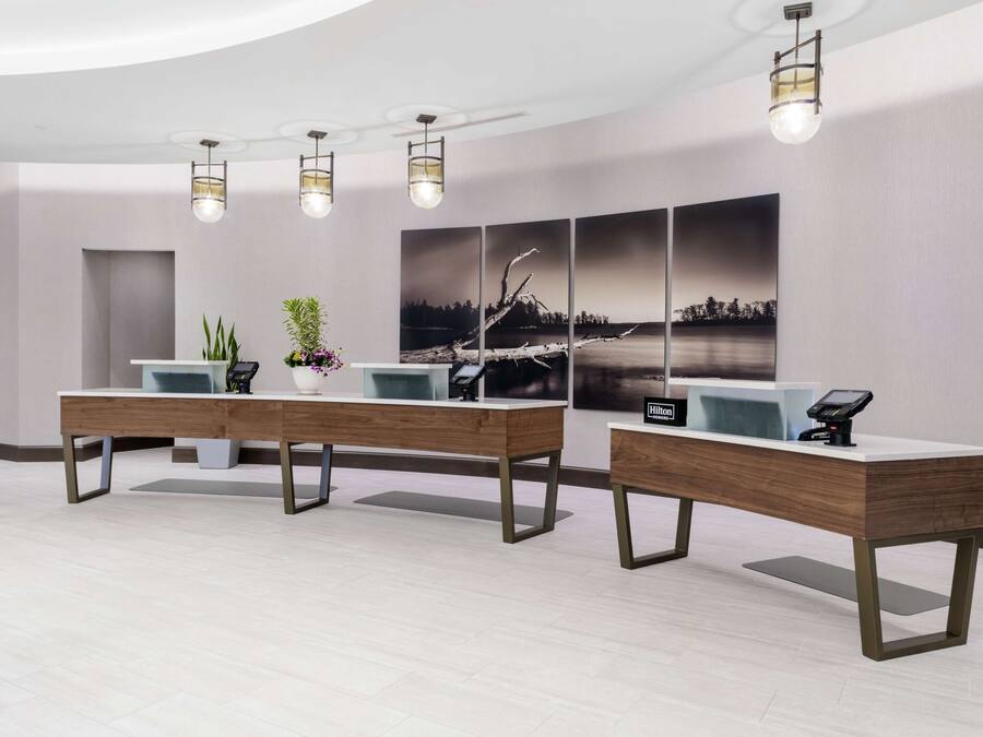A modern reception area with two reception desks, a large landscape painting, and a potted plant.