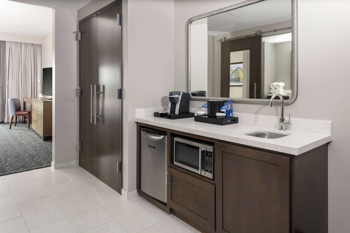 Ein modernes Hotelbad mit integrierter Kaffeemaschine, einem Waschbecken, einer Mikrowelle und einem großen Spiegel.