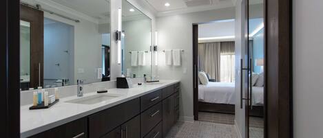 A modern hotel bathroom with a large mirror, dual sinks, and a walk-in closet.