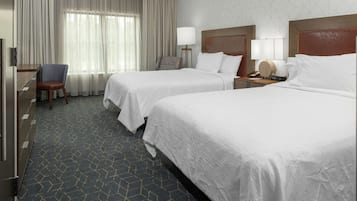 A hotel room with two beds, a desk, a chair, and a window with curtains.