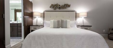 A large bed with a tufted headboard, two bedside tables with lamps, and a wall-mounted light fixture.